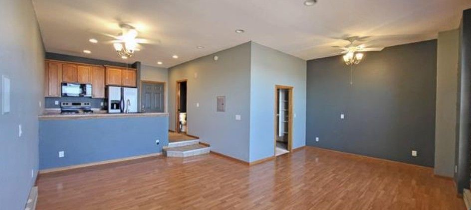 Empty living room with wood floors, gray walls, and open kitchen area with blue half-wall