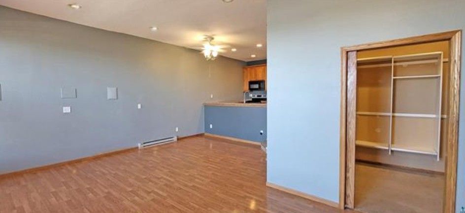 Empty living room with hardwood floor, gray walls, ceiling fan, and open closet door