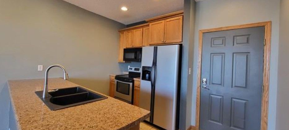 Compact kitchen with granite island, stainless steel appliances, wood cabinets, and gray door