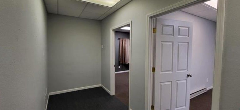 Empty office hallway with gray walls, dark carpet, and open white doors