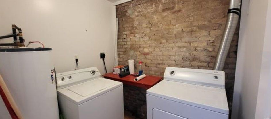 Laundry room with a washer and dryer beside a brick wall and small red utility table
