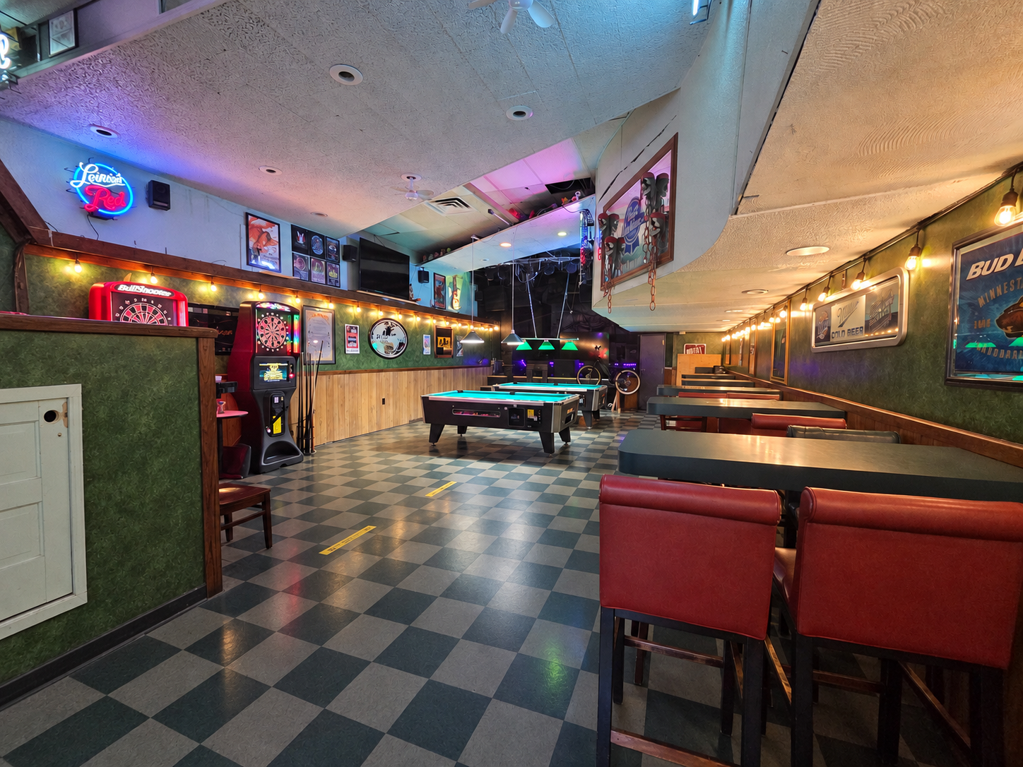Empty bar interior with checkered floor, pool table, red booths, and neon wall lights