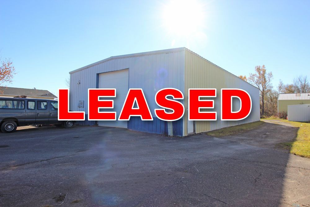 Exterior of a blue and white metal warehouse with a closed garage door, a van, and a sunny sky.