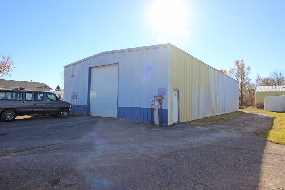 Exterior of a blue and white metal warehouse with a closed garage door, a van, and a sunny sky.