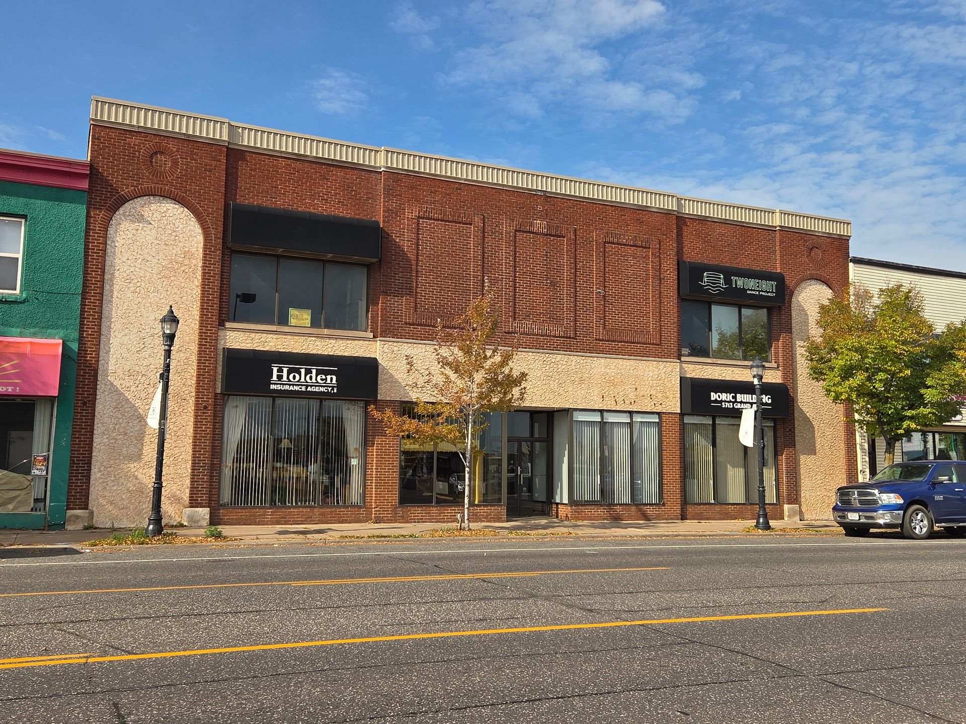 Brick commercial building with storefronts on a street, partly cloudy sky.