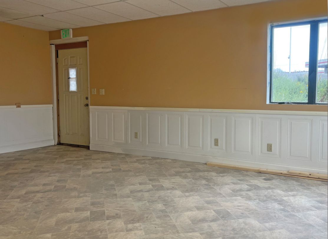 Empty room with tan walls, white wainscoting, a door, and a window, beige linoleum flooring.