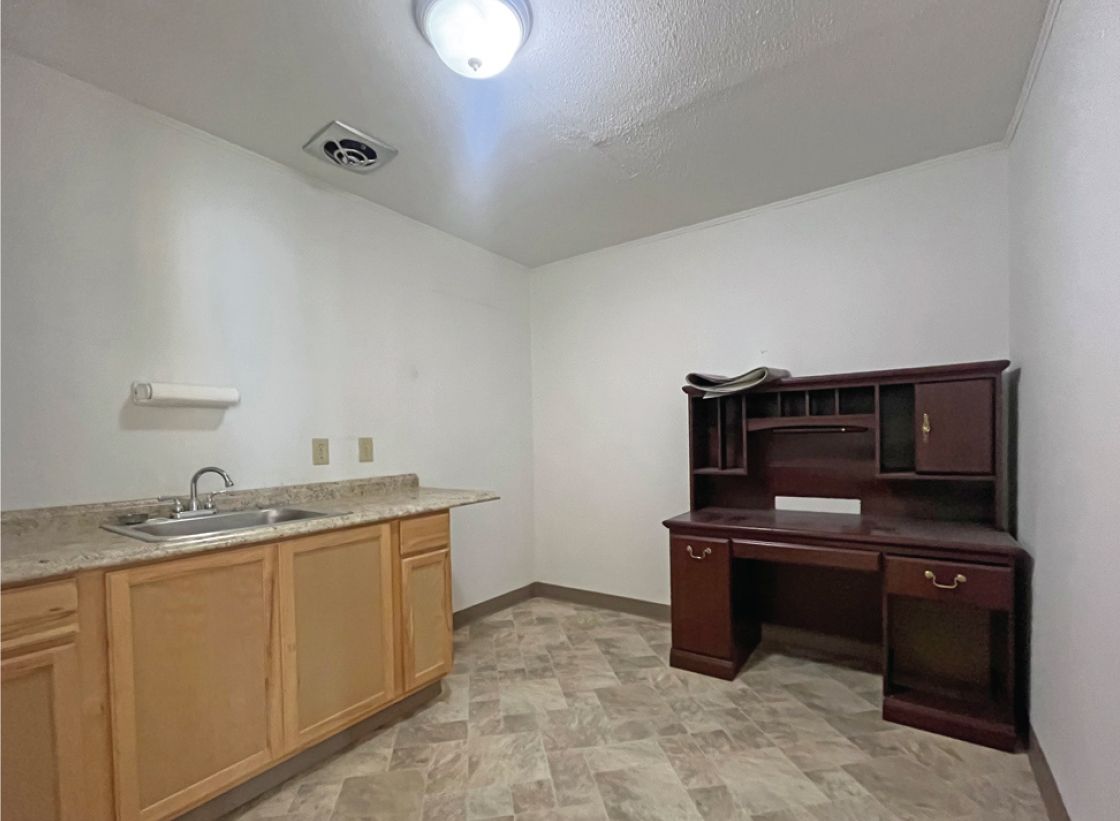 Empty room with a desk, cabinets, and a sink.