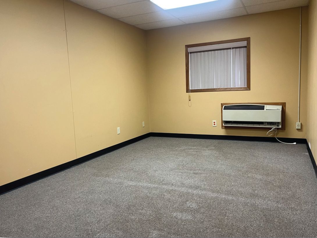Empty beige office room with window, carpet, and air conditioner.