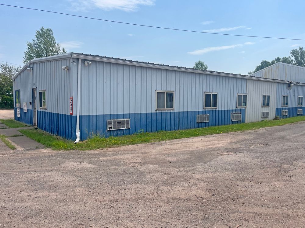 Blue and white metal building with multiple windows and air conditioning units under a blue sky.