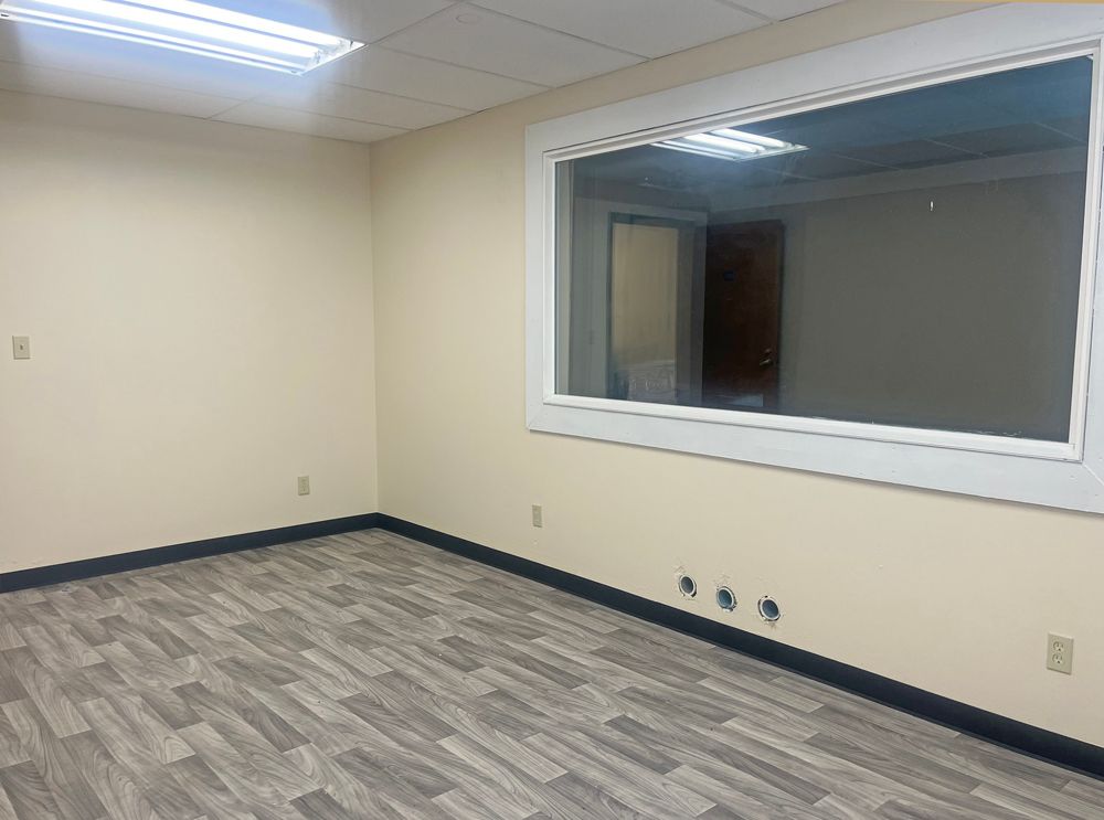 Empty beige office with a large window and wood-look flooring.