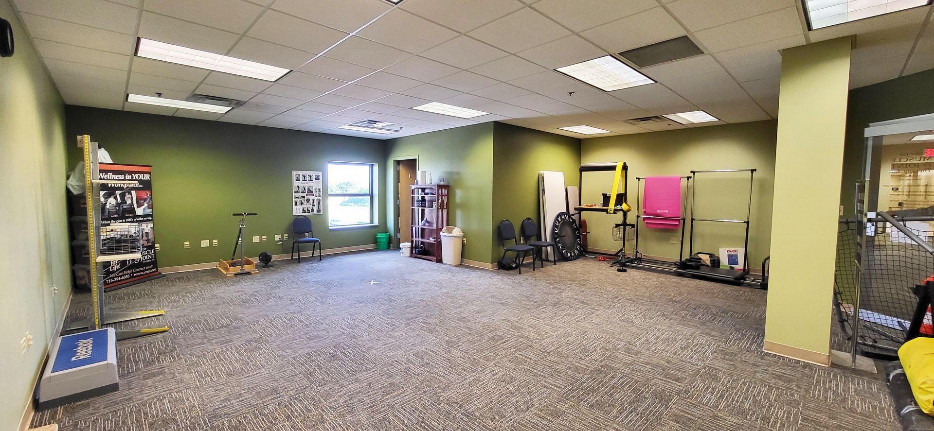 An empty gym with equipment, green walls, beige carpet, and white ceiling lights.