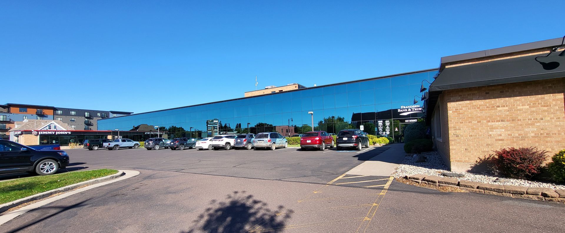 A long building with a reflective glass exterior, cars parked in front, and a blue sky.