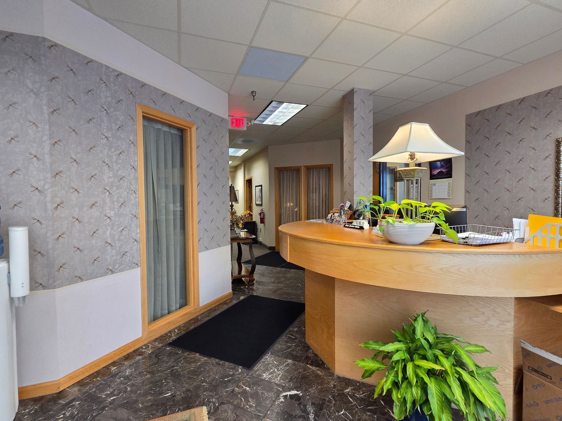 Reception area with a wooden counter, plants, and patterned wallpaper.