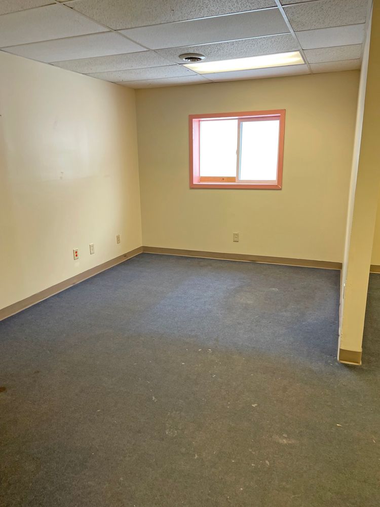 Empty room with blue carpet, beige walls, small window with pink trim.