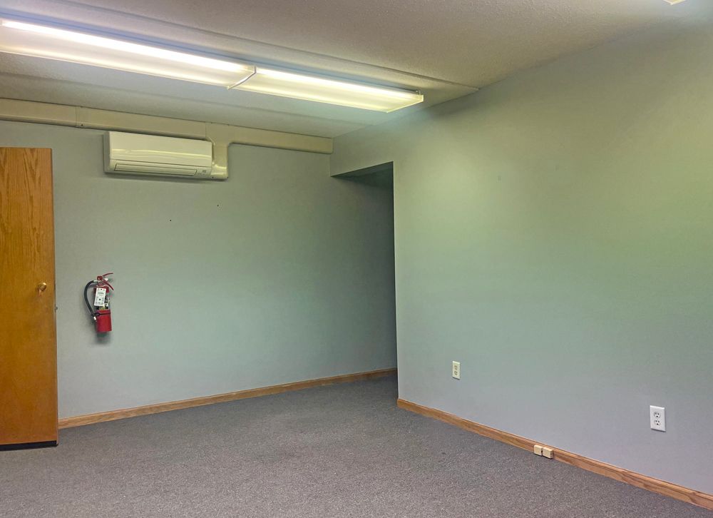 Empty room with gray walls, carpet, and door. Fire extinguisher on wall.