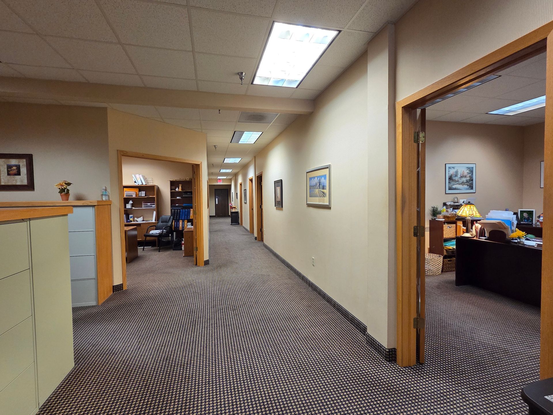 Office hallway with doors, art on walls, and patterned carpet.