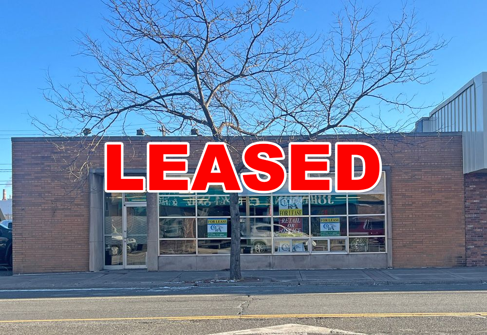 A brick building with a lot of windows and a tree in front of it with LEASED sign
