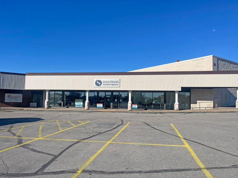 Exterior view of the Solutions Insurance Agencies in a strip mall with a blue sky.