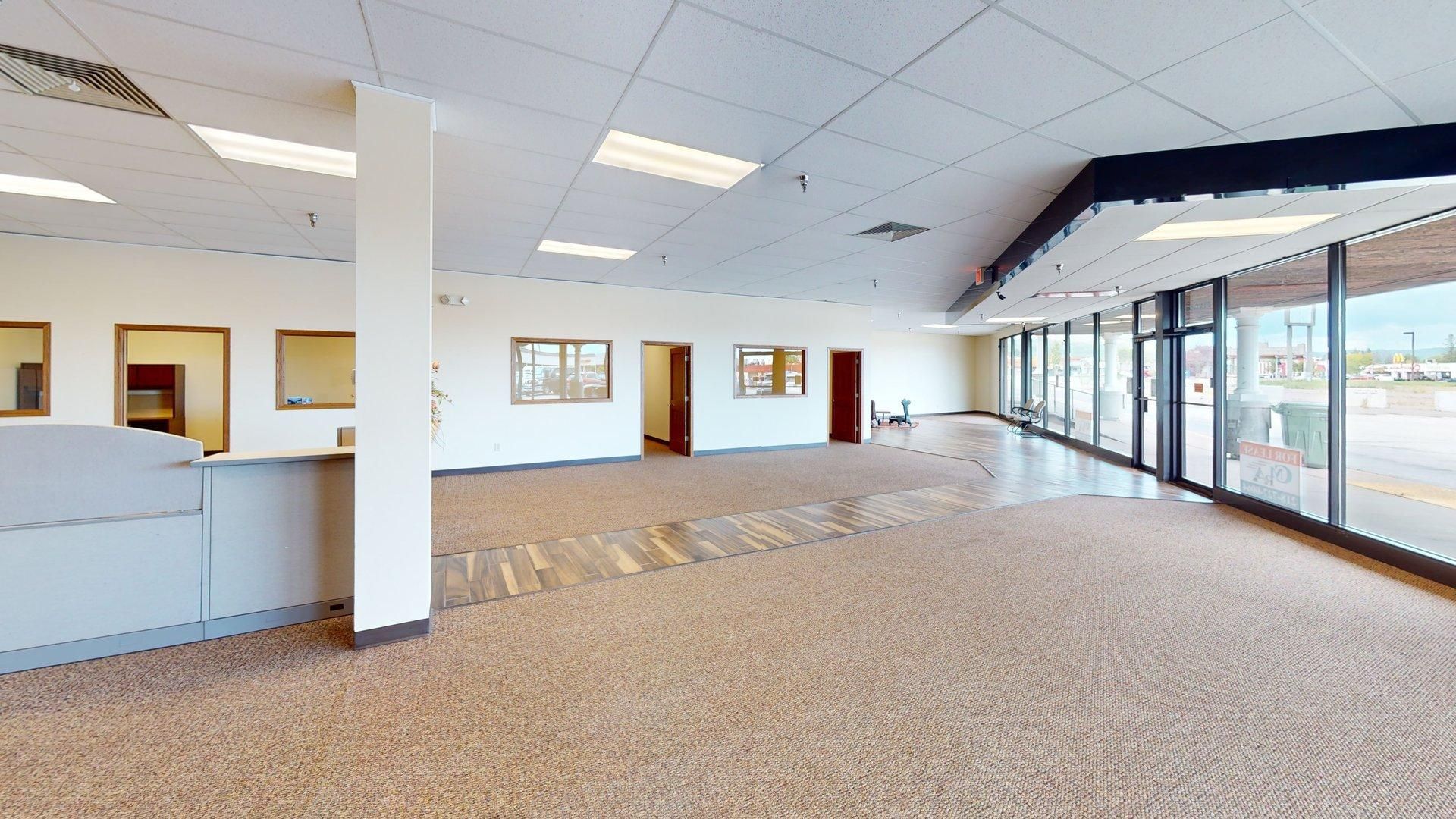 Empty office space with carpeted floors, large windows, and a column.
