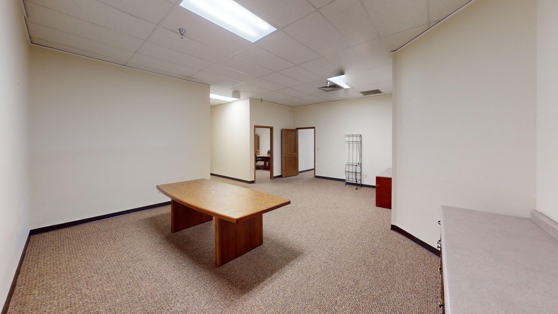 Empty office space with a large wooden table and neutral carpet.