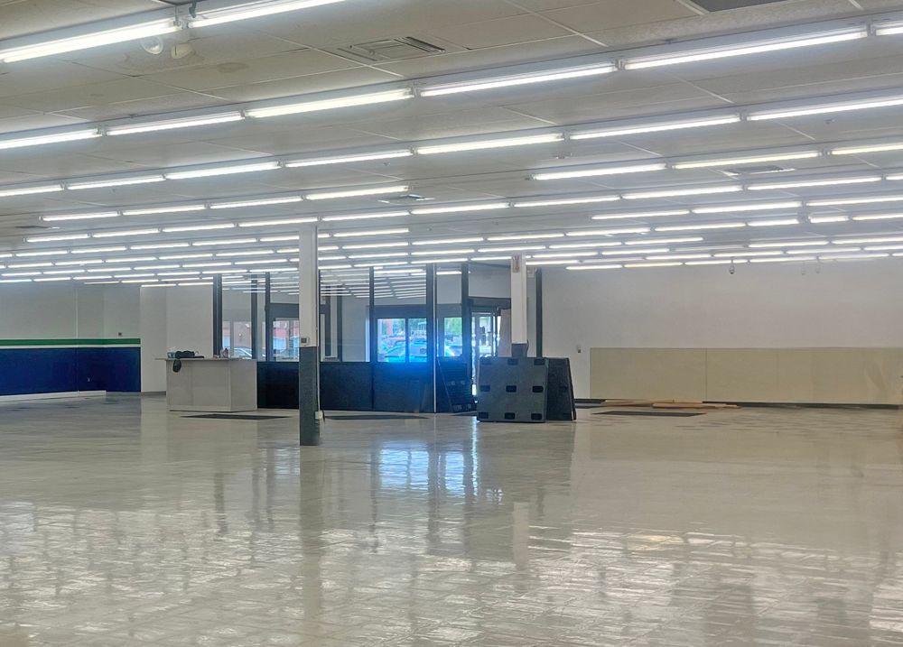 Empty, spacious retail interior. Fluorescent lights shine on a gray floor. Doors are visible in the distance.