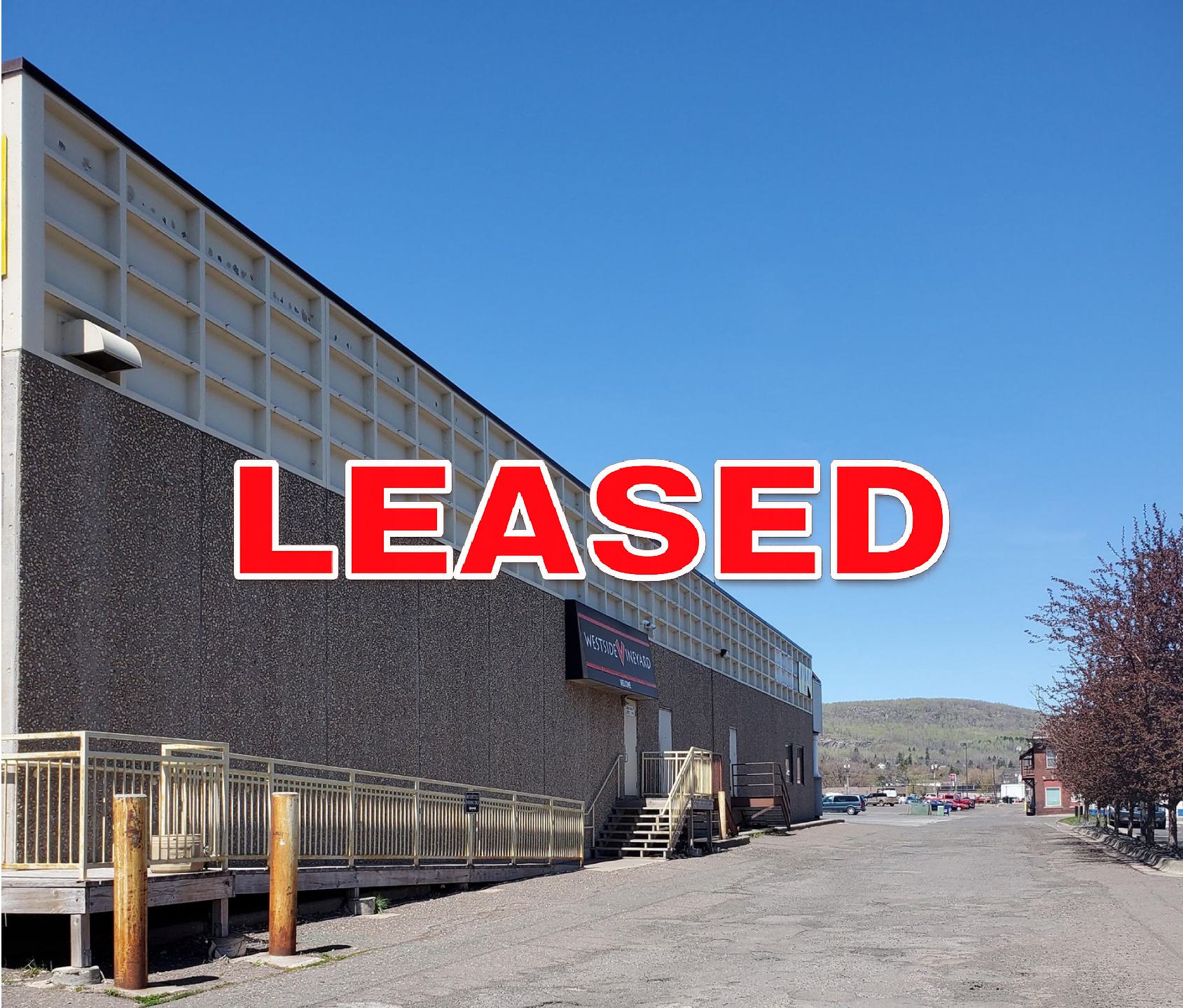 Large building with red “LEASED” sign over a gravel lot under a blue sky