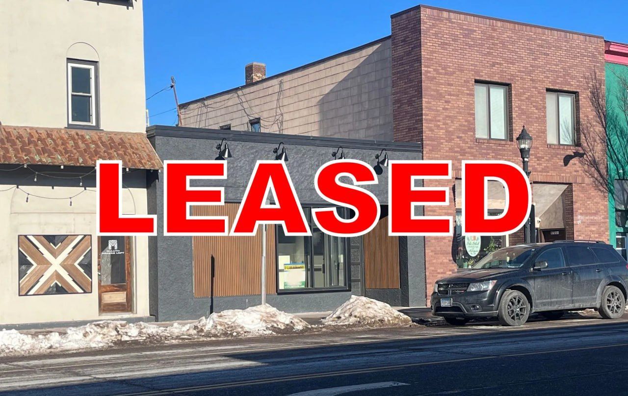 Brick storefronts on snowy street with a parked SUV, overlaid with large red “LEASED” text
