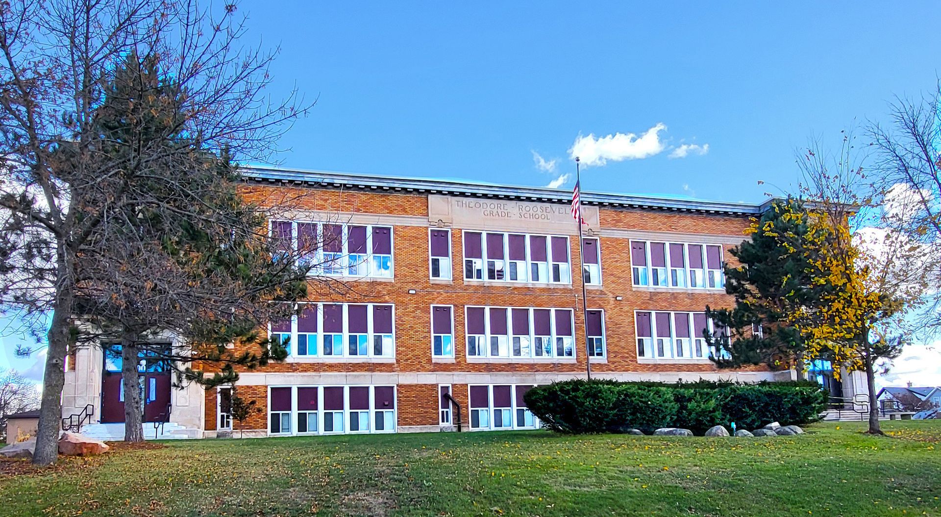 Brick school building with white windows and autumn trees under a blue sky