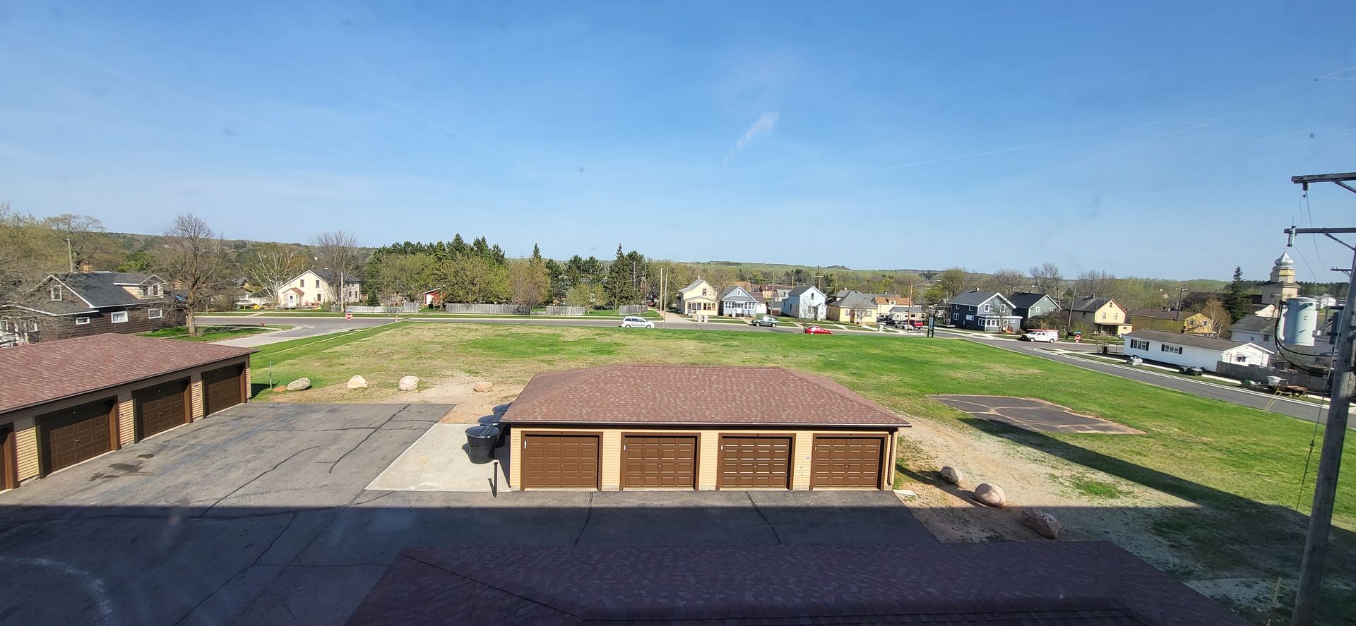 Sunny view of a grassy vacant lot with scattered houses and a red-roofed building in the foreground