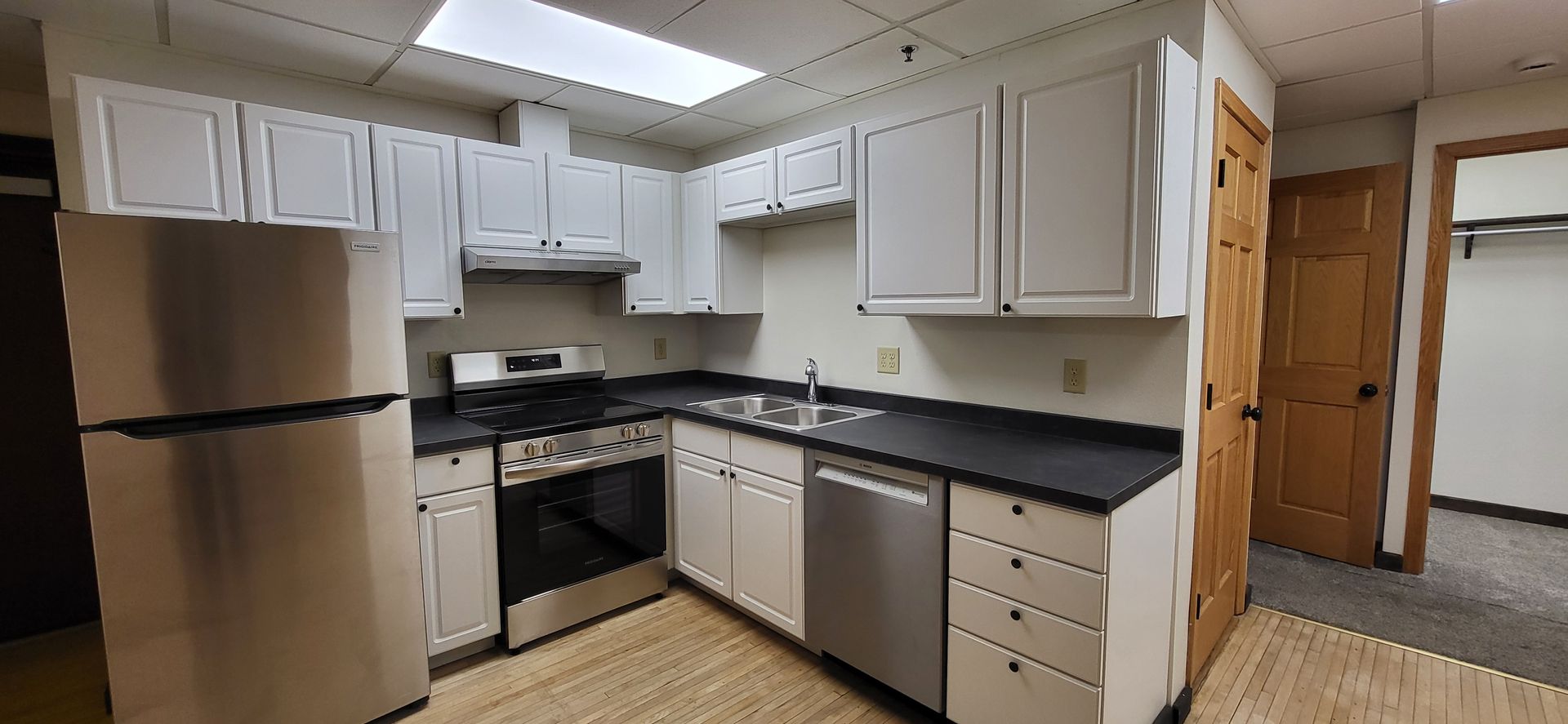 Bright kitchen with white cabinets, black countertops, stainless steel appliances, and wood floor.