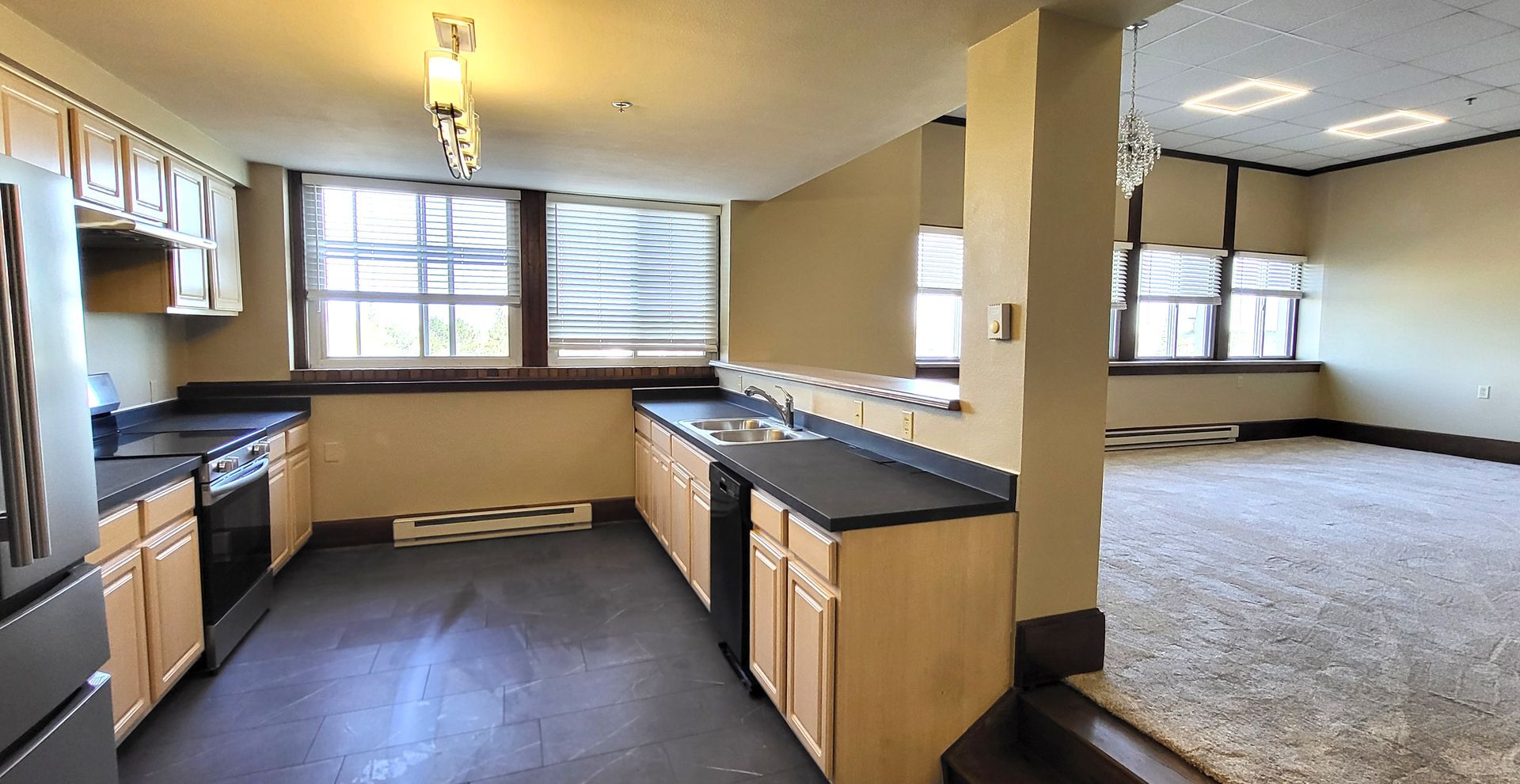 Empty kitchen and carpeted living area in a bright open-plan room with windows and a central island