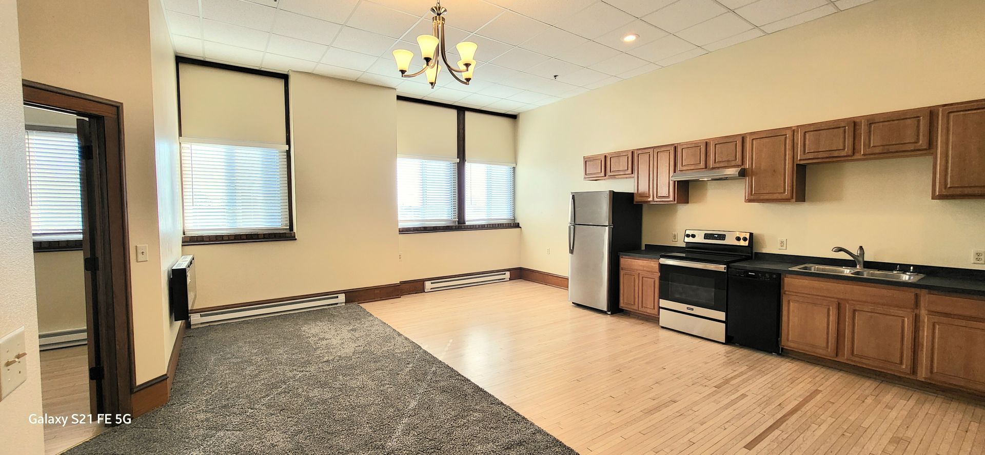 Empty apartment kitchen and living area with wood cabinets, black countertops, and large windows