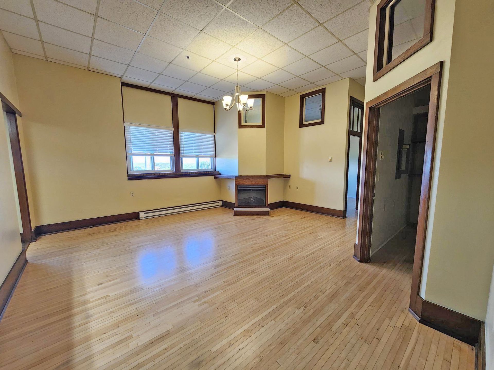Empty room with hardwood floors, beige walls, windows, and a ceiling light fixture.