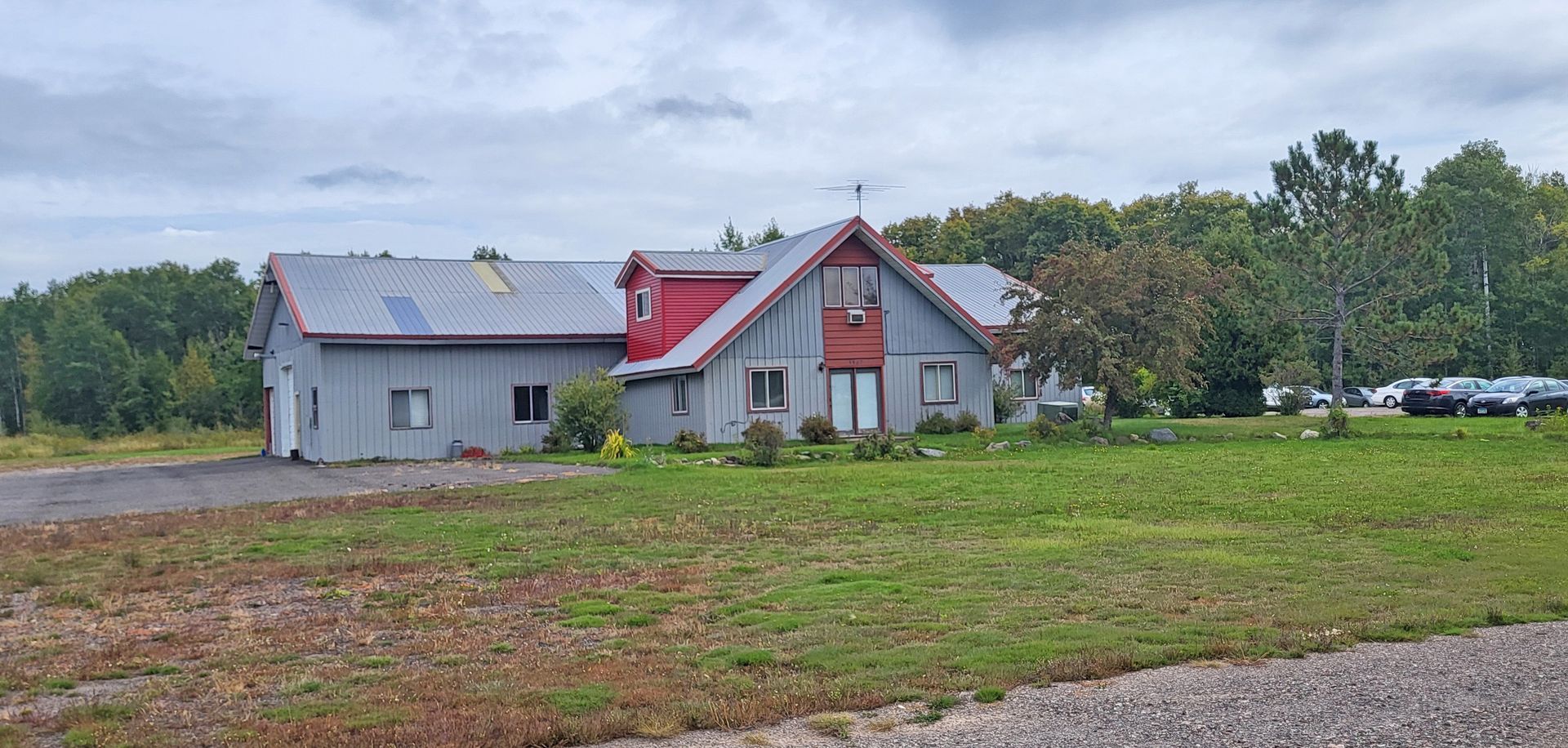 Rural house and barn with red roof in a grassy field under cloudy sky