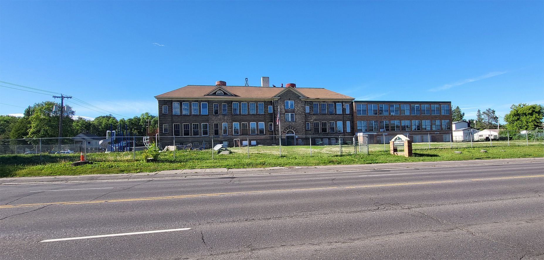 Wide brick building with blue windows beside a road under a clear sky