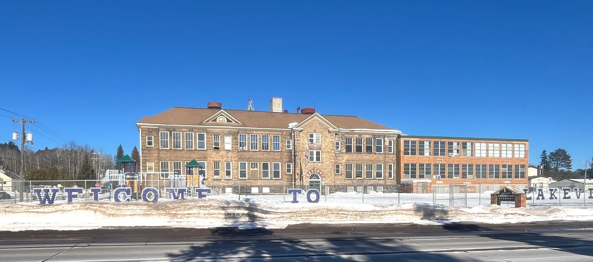 School building with a blue sky, snow on the ground, and letters visible in front of the building.