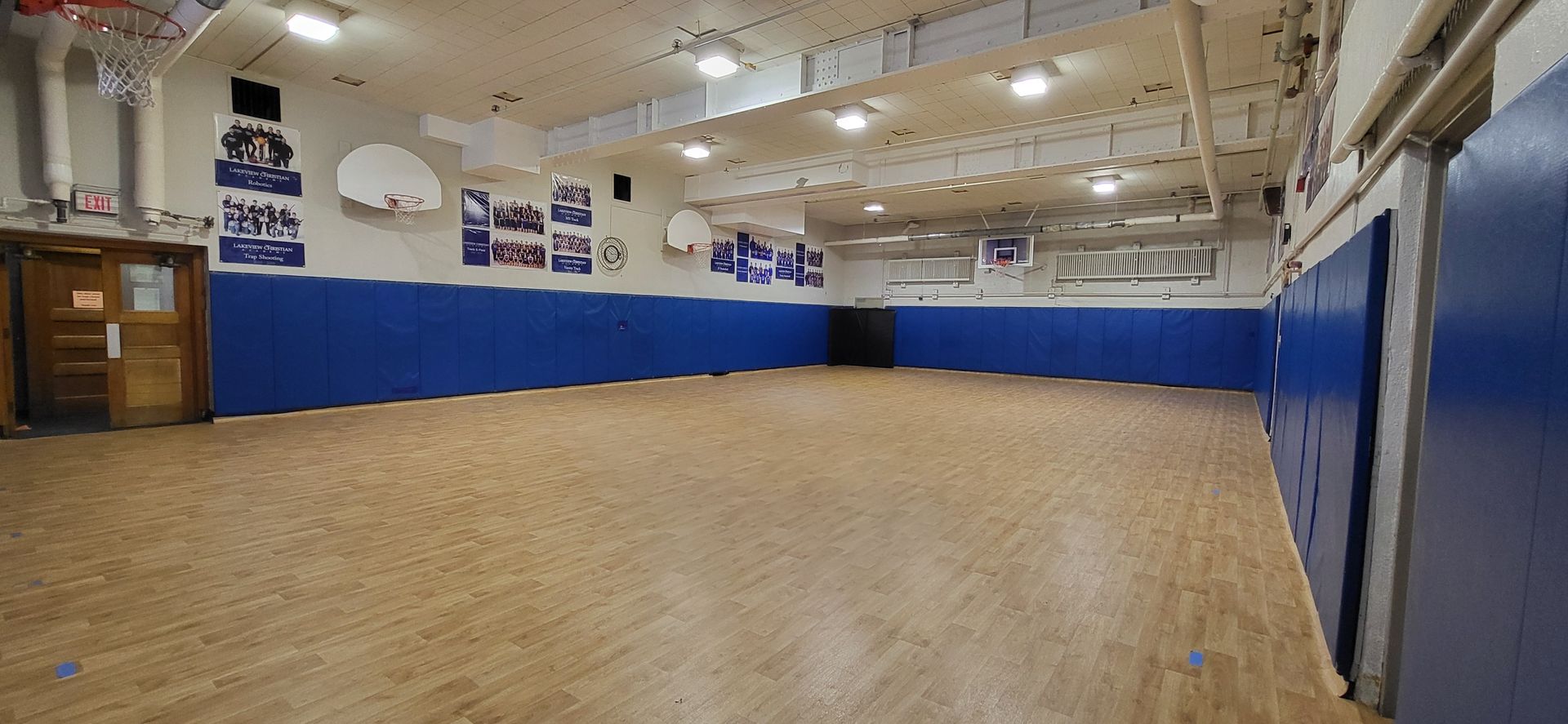 A school gymnasium with a wooden floor, blue padded walls, and basketball hoops.