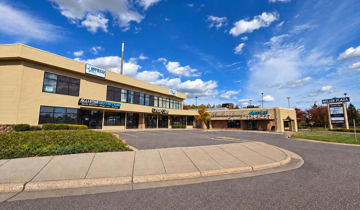Low-rise beige office building with blue awnings and a curved driveway under a bright blue sky