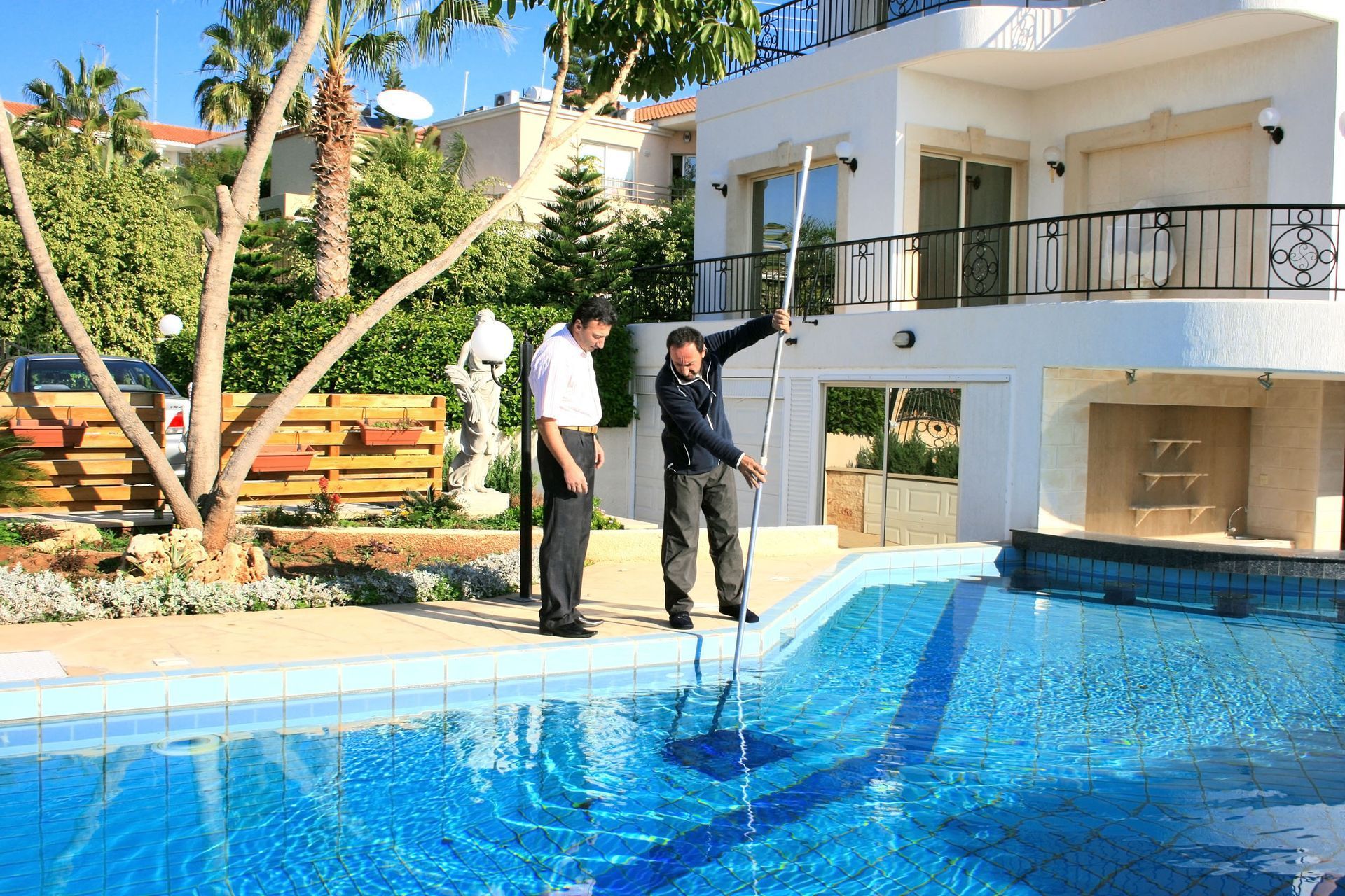 Two men measuring pool depth with a pole at a house with a pool.