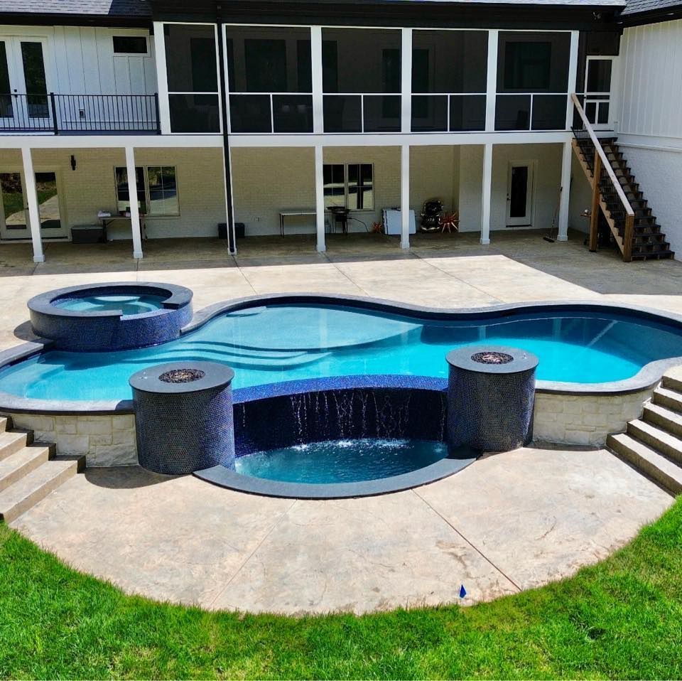 Backyard pool with a hot tub and fire features, with a two-story white house in the background.