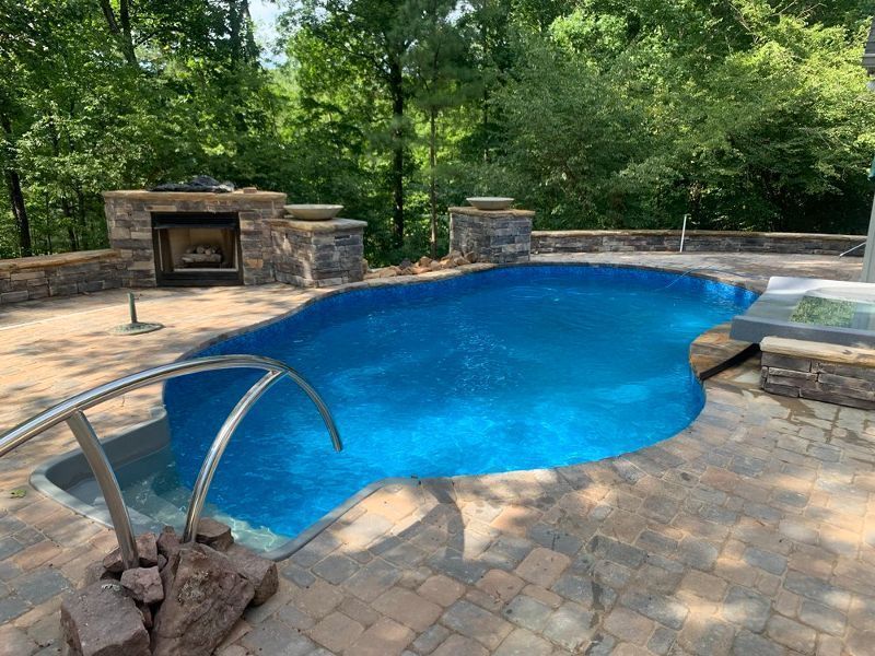 Outdoor swimming pool with blue water surrounded by stone patio and retaining walls. Fireplace.