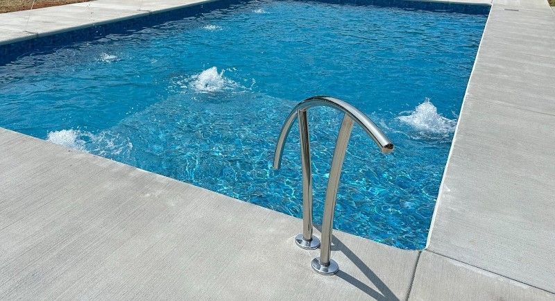 Swimming pool with concrete deck and stainless steel handrail. Bubbles in the blue water.