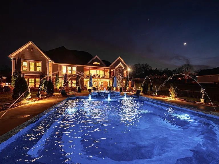 Swimming pool with rock waterfall feature, palm trees, and a house in the background.