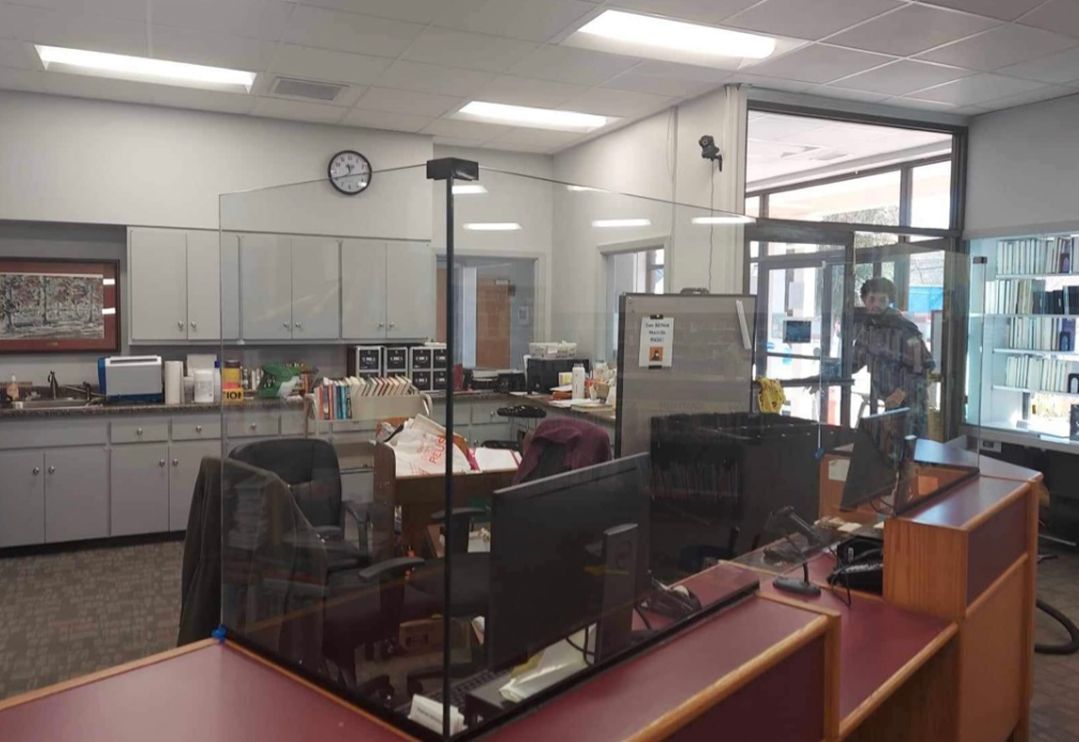 a man is standing in a room with a glass barrier between two desks