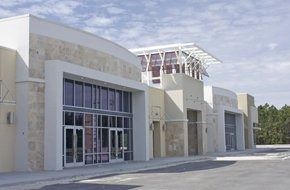 Modern beige and white building with glass storefronts and a parking lot.