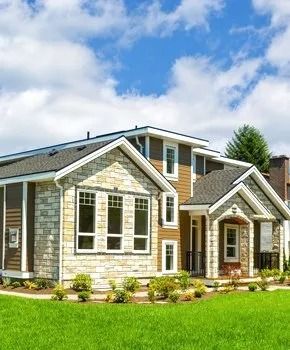 Two-story house with stone and brown siding, white trim, and a green lawn under a blue sky with clouds.
