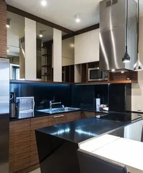 Modern kitchen with black countertops, wood cabinets, stainless steel appliances, and mirrored backsplash.