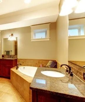 Bathroom with a tub, sink, and window. Beige walls and brown vanity, counter, and tiles.