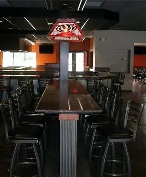 Bar area with high-top seating, dark floor, and an illuminated light fixture with a logo hanging from the ceiling.