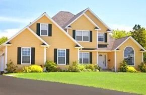 Yellow house with black shutters, green lawn, blue sky.